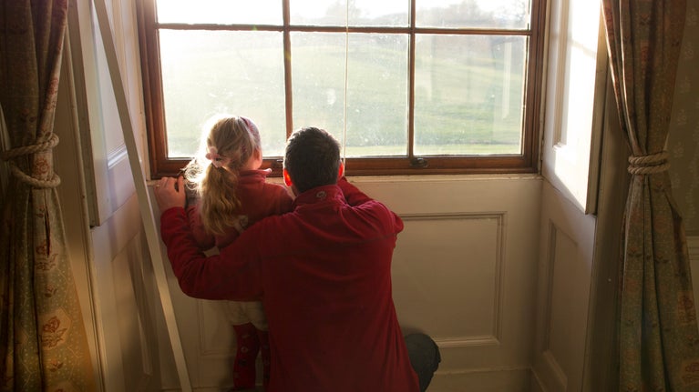 A father and child peering out of a window inside Berrington mansion.